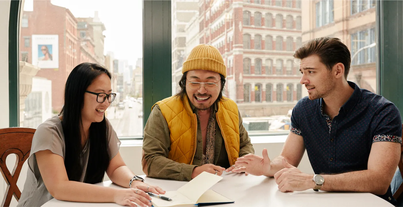 Three people happily working at a desk in an office.