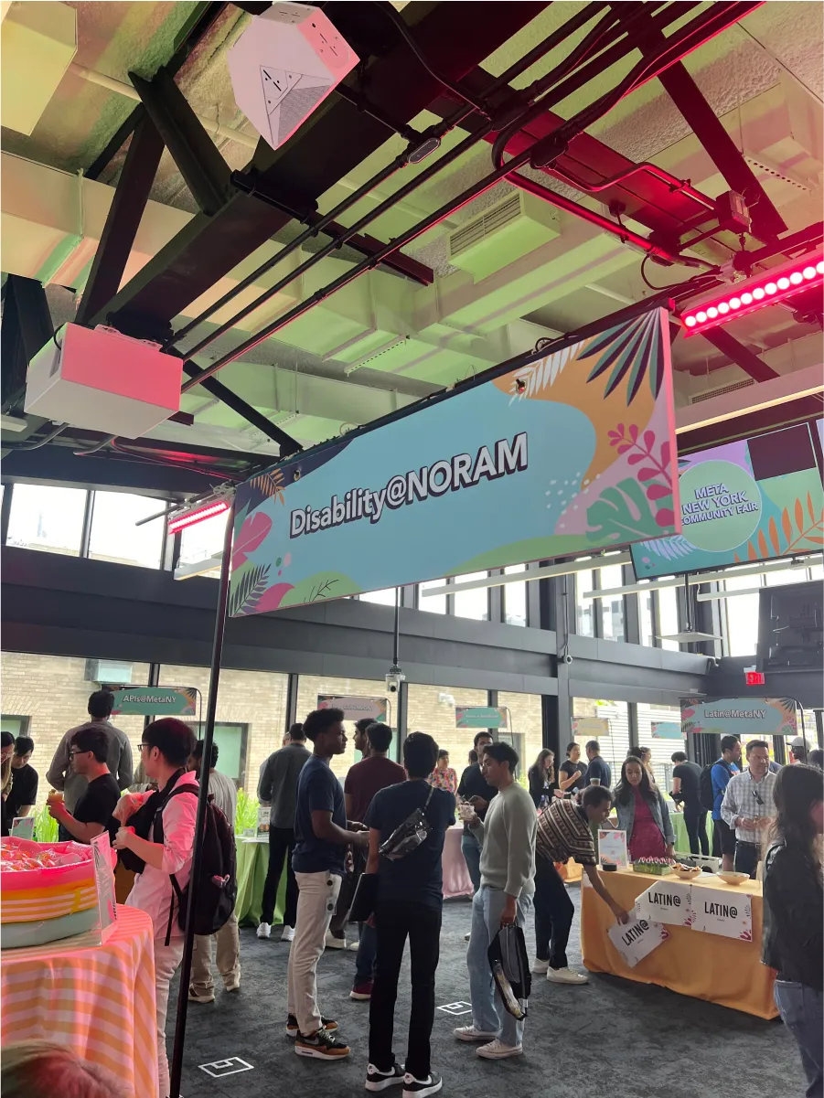 Neon‑lit indoor event with “Disability@NORAM” banner, tables, and attendees socializing at a vibrant community fair.