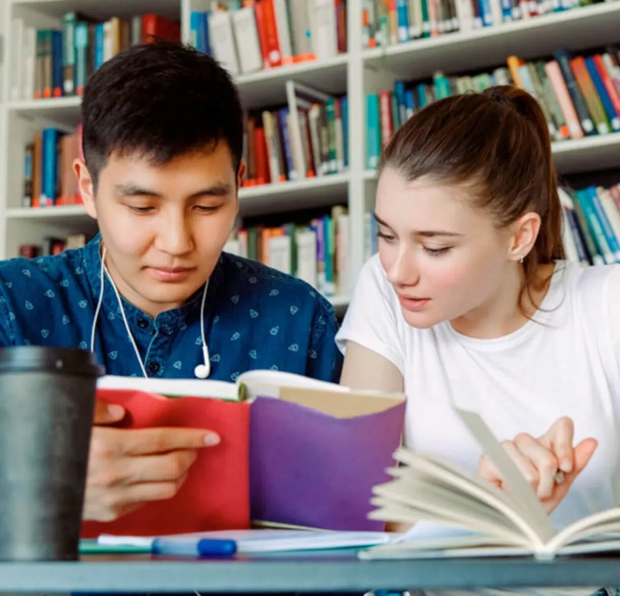 Due studenti che studiano insieme a un tavolo della biblioteca, con dei libri aperti.