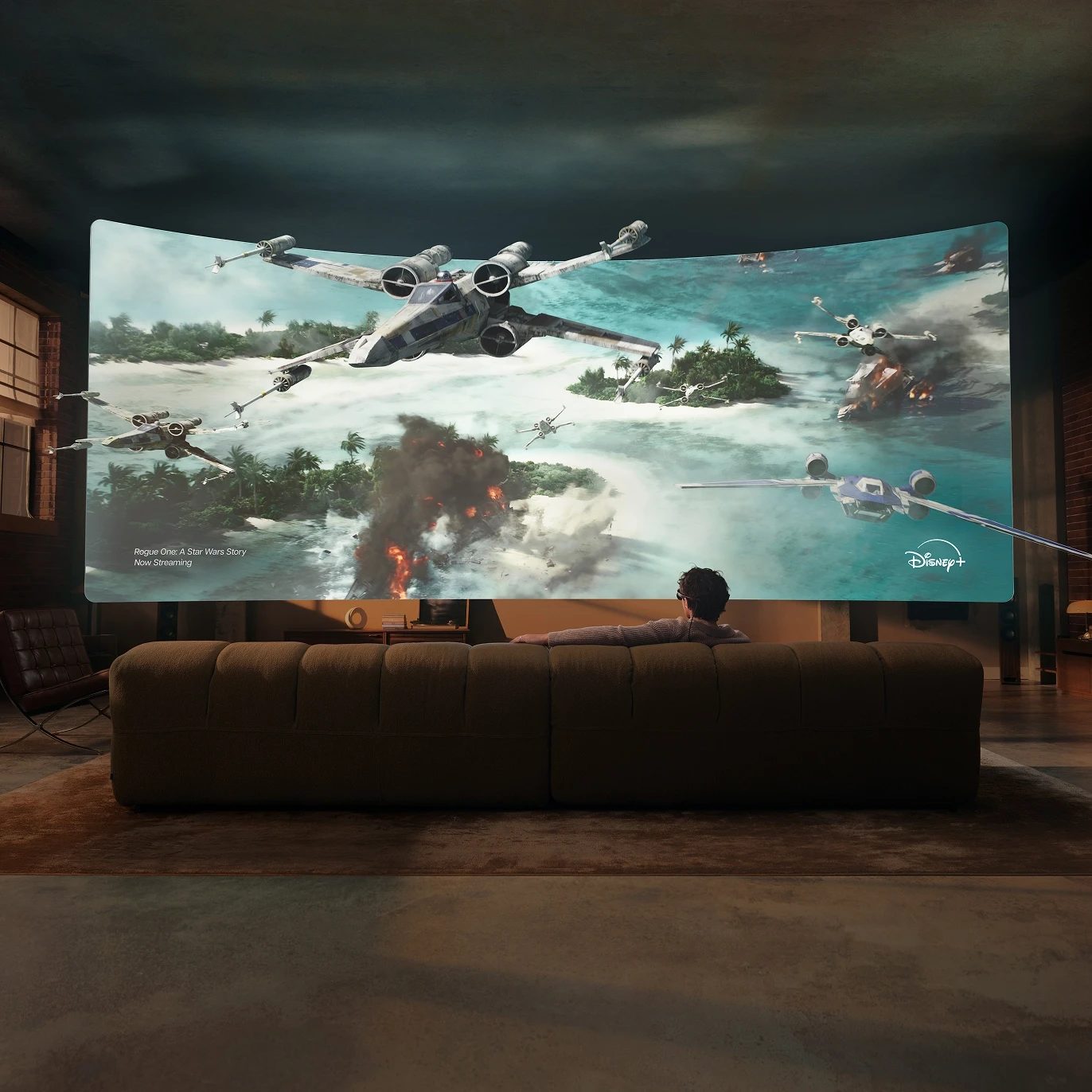 Person on a sofa watching a movie on a cinema-sized screen that fills the wall of their living room.