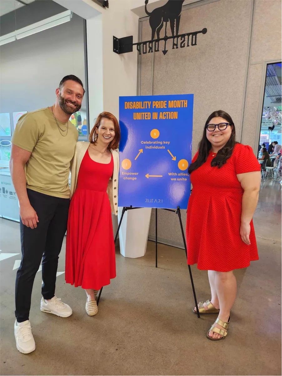 Three people stand beside a blue poster that reads “DISABILITY PRIDE MONTH – UNITED IN ACTION” with a three-step action plan.