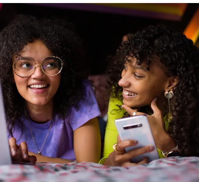 Deux jeunes sourient et se regardent en tenant un téléphone intelligent, assis côte à côte.