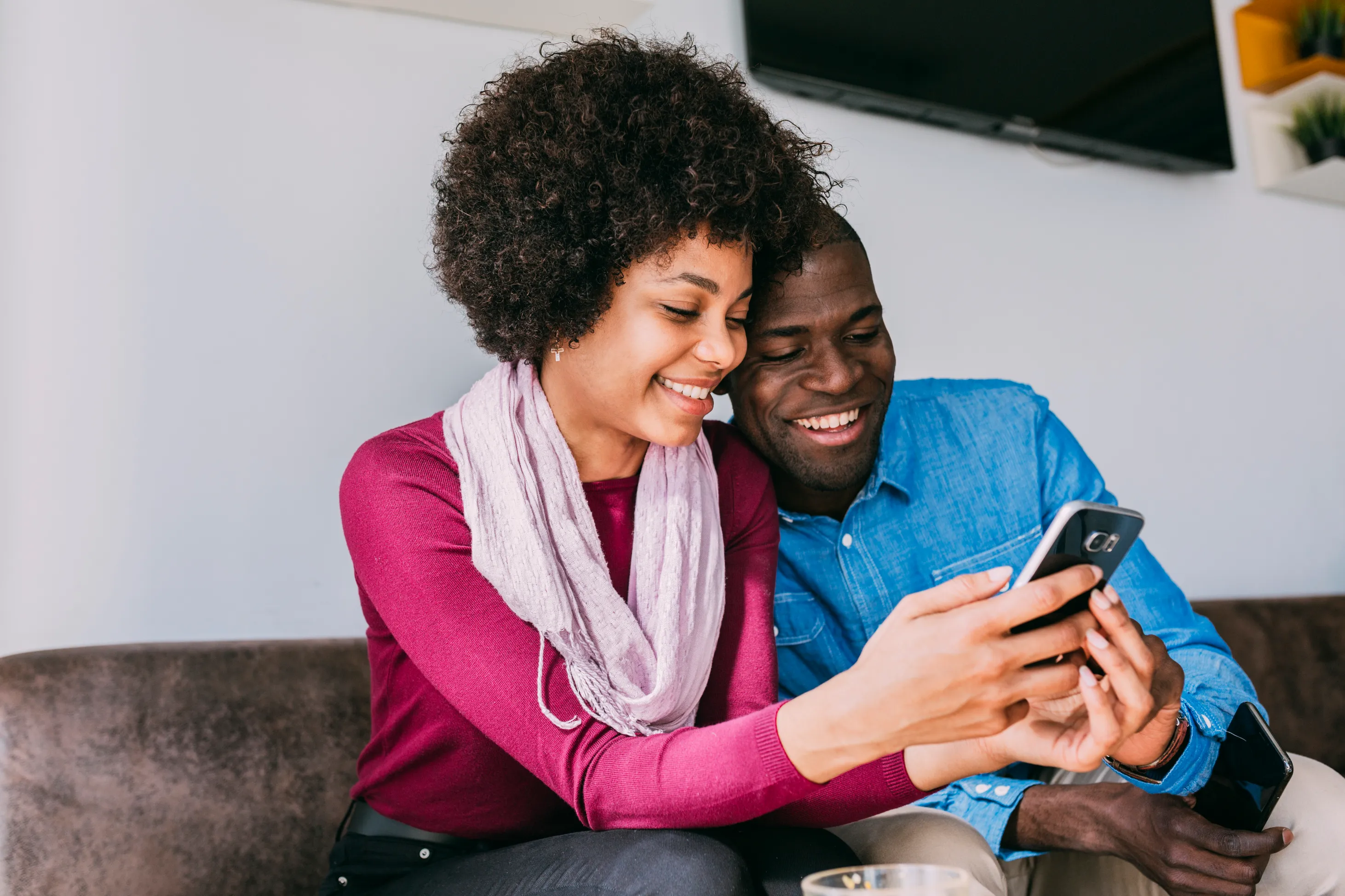 Two people sitting together and smiling while looking at a phone.