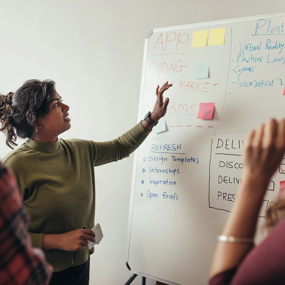 A woman collaborating with colleagues at a whiteboard to plan and manage complex technical programs using AI-powered tools.