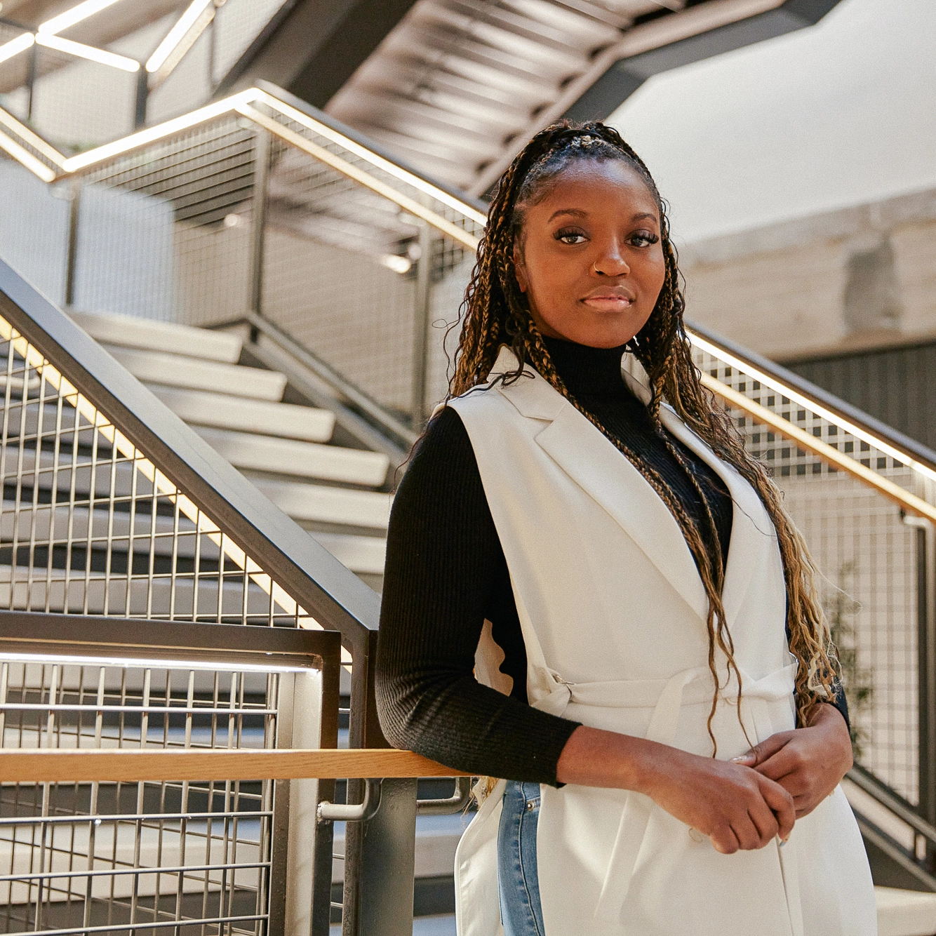 A woman standing near stairs, looking toward the camera.