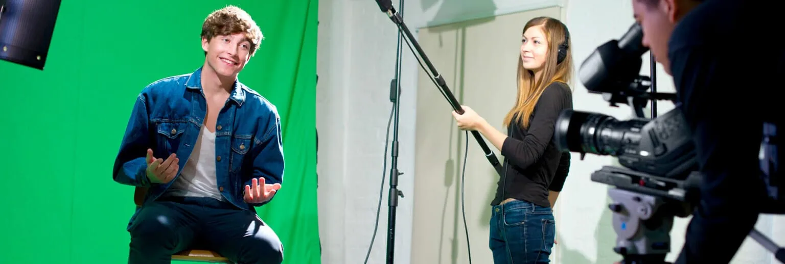 Persona che parla di fronte a un green screen mentre una troupe lo riprende con una telecamera e un'asta telescopica.