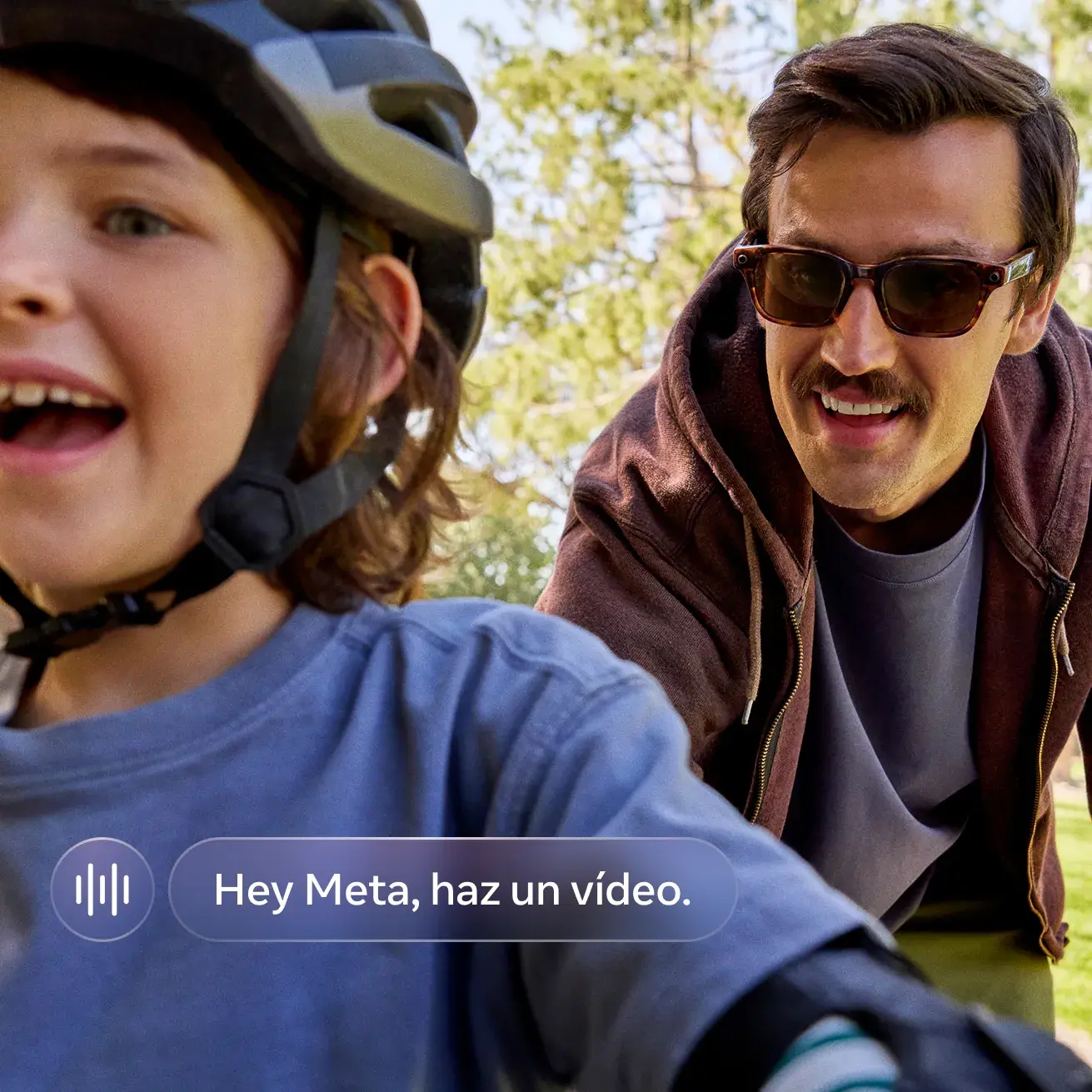 A man wearing Meta glasses rides a bike alongside a smiling young child in a helmet on a tree-lined trail.