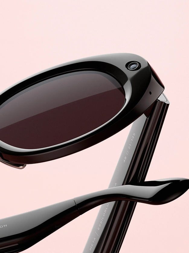 Nahaufnahme der Meta AI Glasses, die die integrierte Kamera am Gestell zeigt, vor einem weichen rosa Hintergrund.