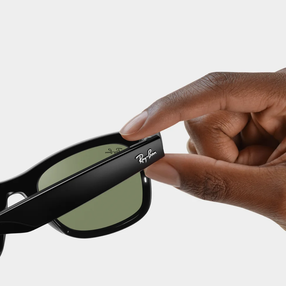 A hand holding a pair of sunglasses with the Ray-Ban logo.