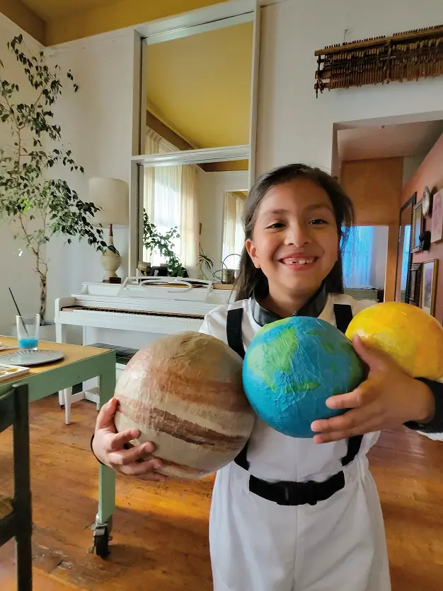 A smiling child holding model planets in a living room.
