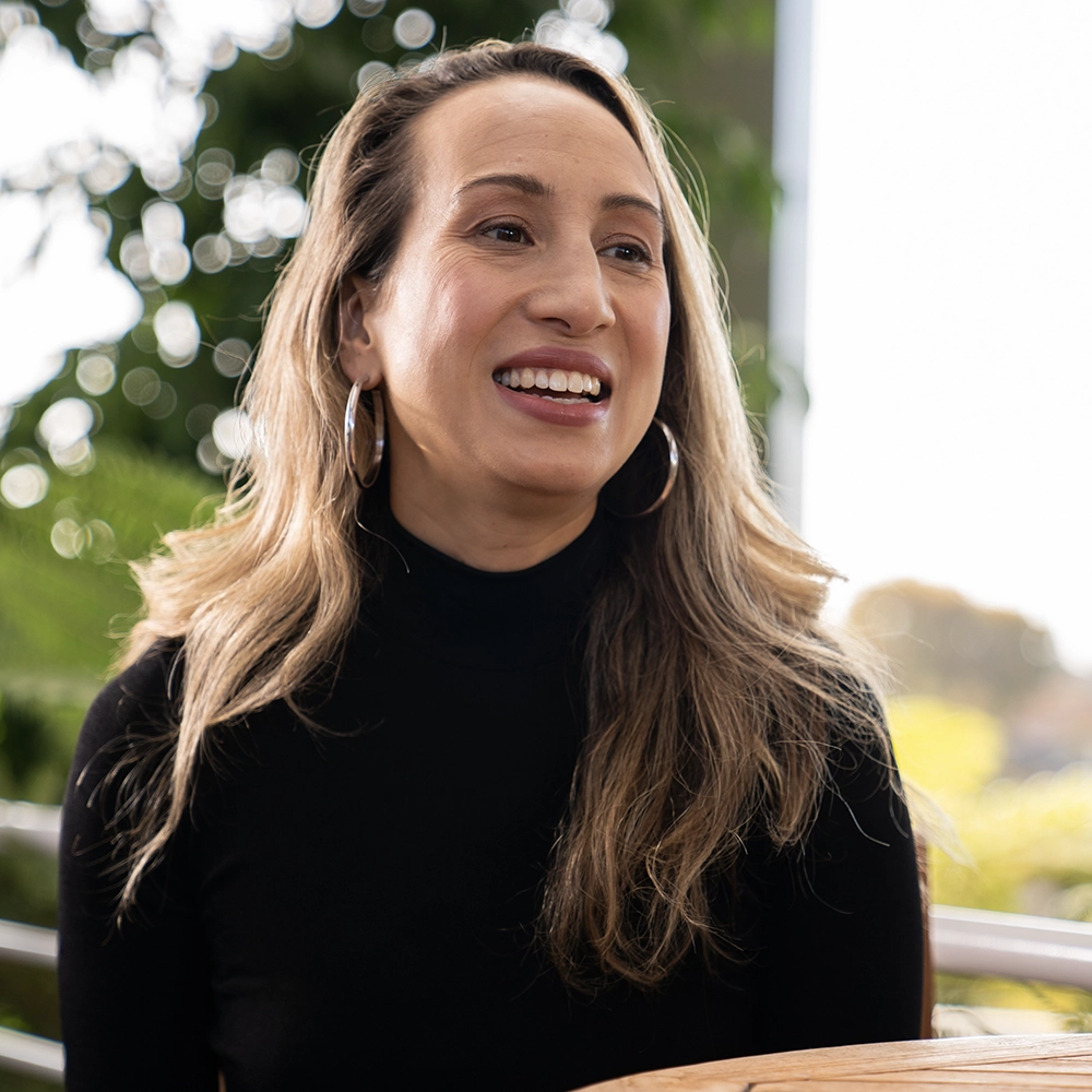 A woman in a black turtleneck looking diagonally off-camera while speaking.