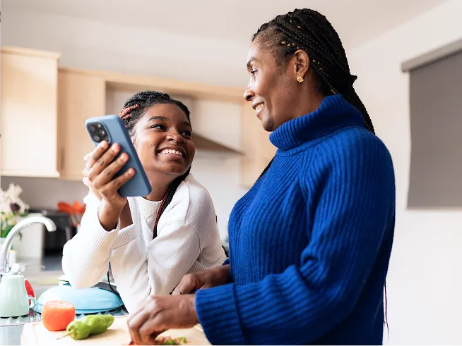 Un adulto e una teenager che si sorridono vicino al bancone della cucina mentre tengono in mano un telefono.