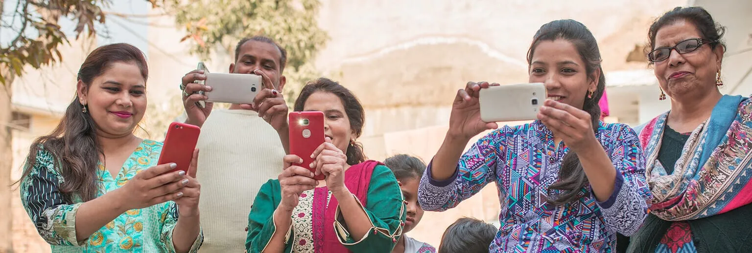 ग्रुप में खड़े लोग, जो मुस्कुरा रहे हैं और स्मार्टफ़ोन से फ़ोटो ले रहे हैं.