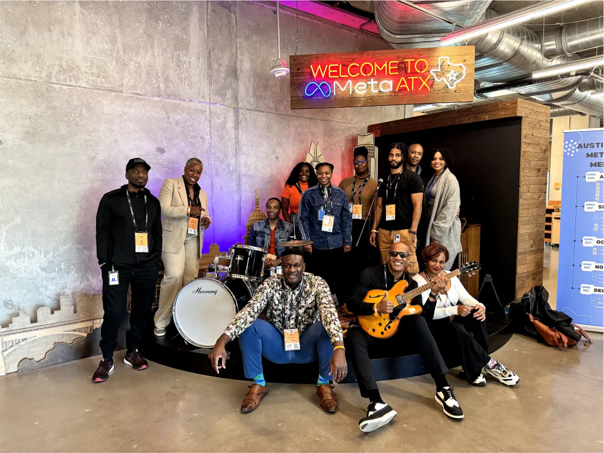 A group of ten people posing in front of a “WELCOME TO Meta ATX” neon sign with a drum set and a guitar, wearing lanyards with badges.