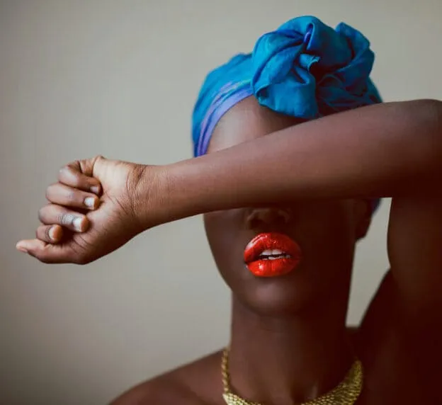 Primer plano de una persona con los labios pintados de un color brillante, que se cubre parte del rostro con el brazo.