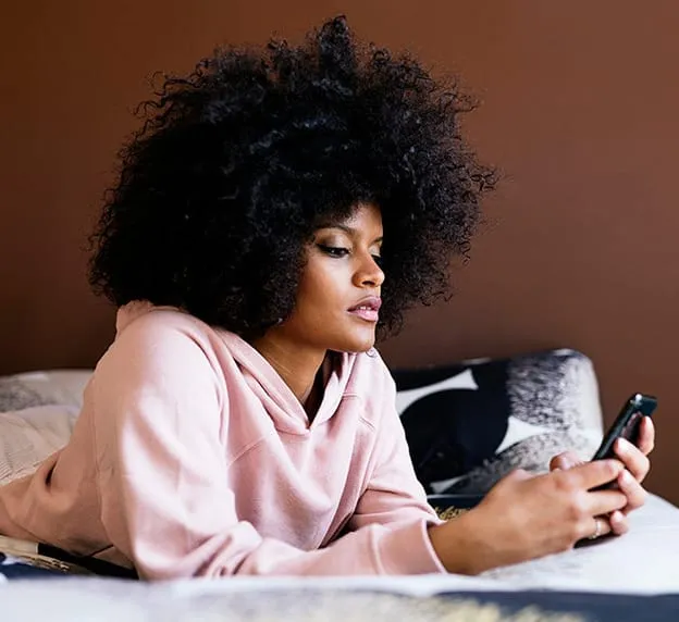 Person in a hoodie looking at a phone while seated indoors.