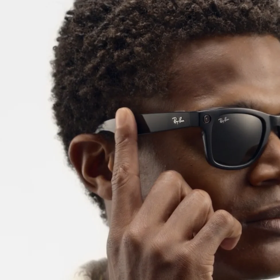 A person wearing sunglasses with the Ray-Ban logo on the frame touching the glasses arm.