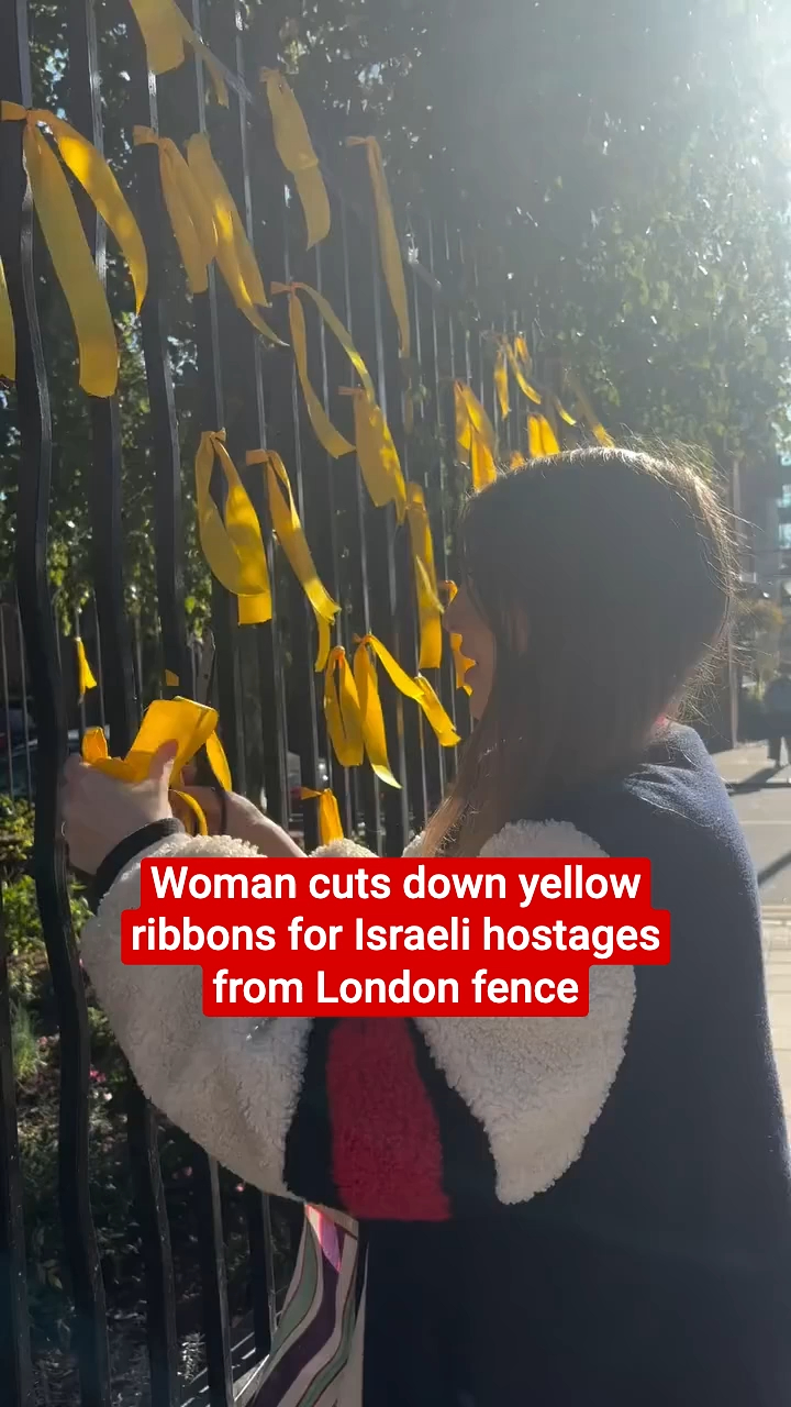 A woman cutting down yellow ribbons for Israeli hostages on a fence ...