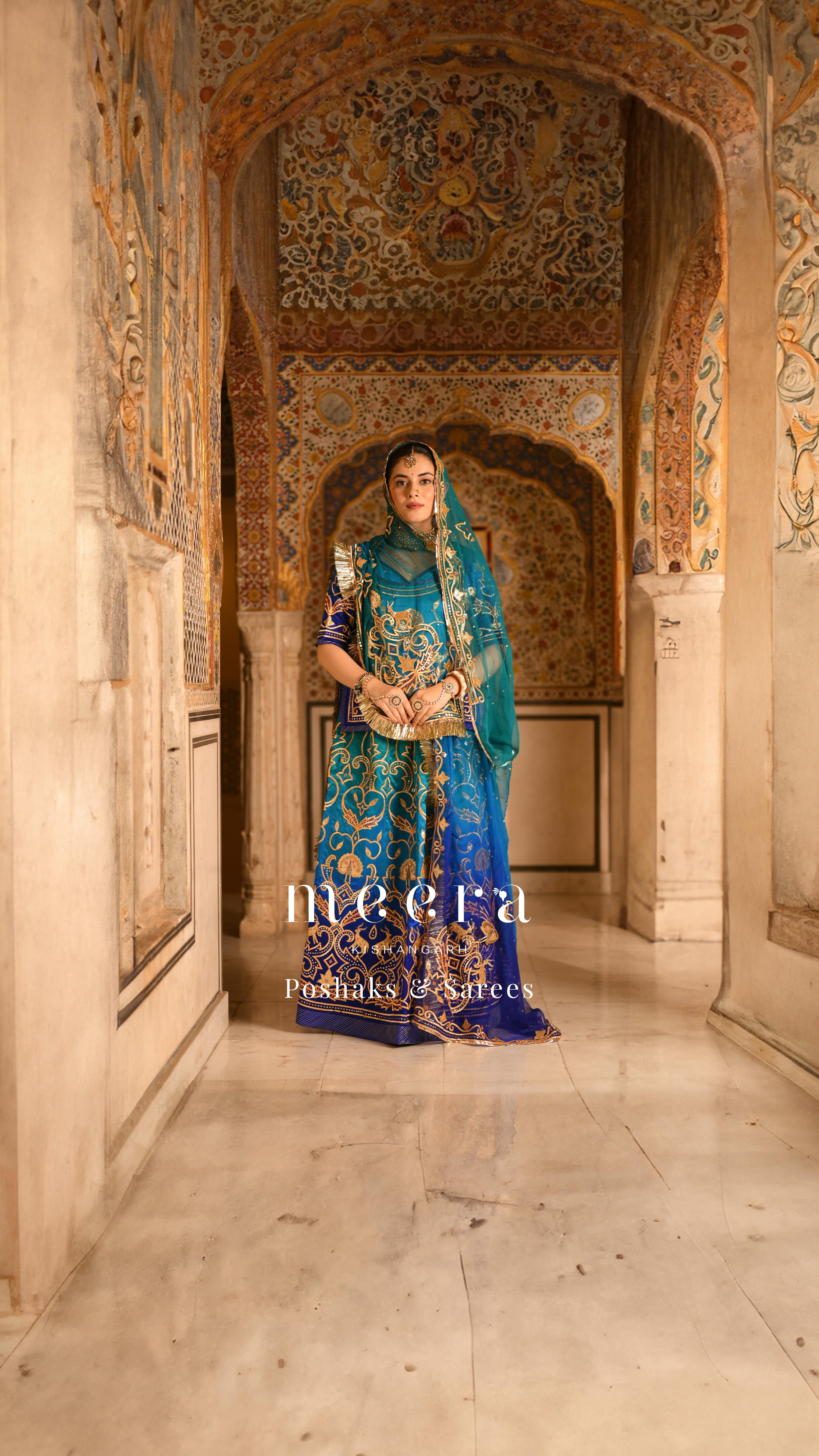 blue rajputi dress This peacock blue-green poshak is a unique masterpiece, adorned with intricate sikhiya and laffa work depicting a mesmerizing palace garden with colourful thread embroidery . This Peacock colour