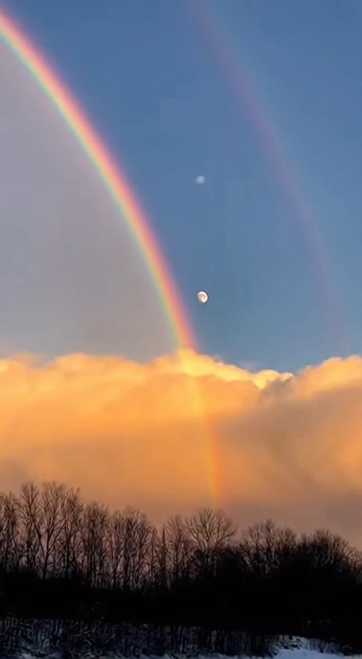 A perfect rainbow arches the sky as the Moon quietly drifts beneath it ...