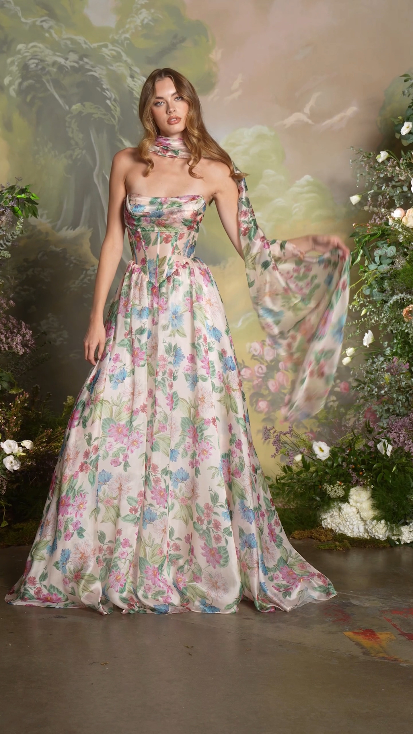 This romantic A-line gown brings garden-party elegance to life with its soft floral print and flowing silhouette. Featuring a strapless draped neckline and structured sheer mesh corset bodice, the 