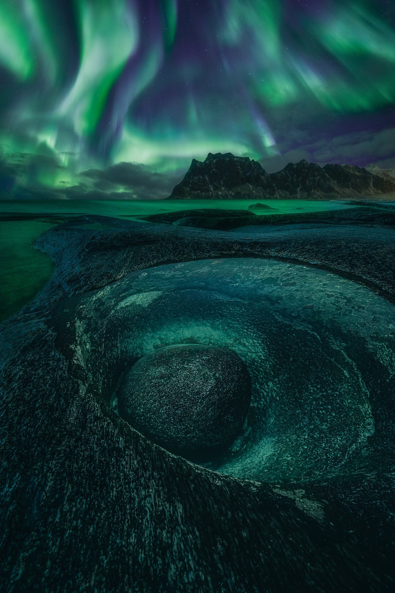 The Northern Lights shine over the rocks of Uttakleiv beach in