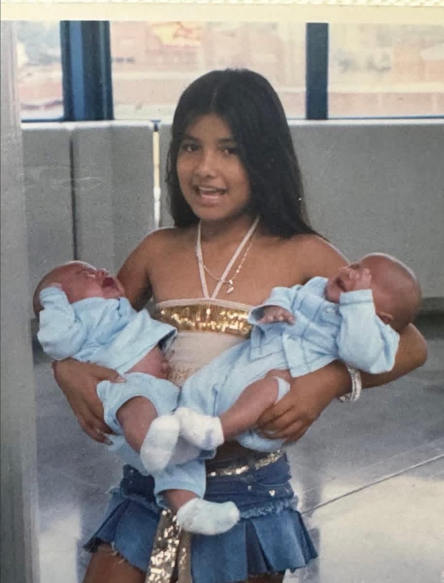 Picture 1: she is carrying her twin brother Picture 2: she is