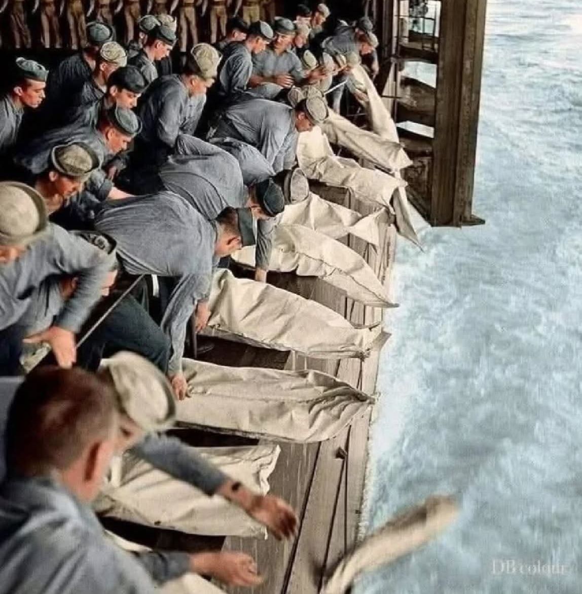 A colorized photograph of a mass burial at sea aboard the USS