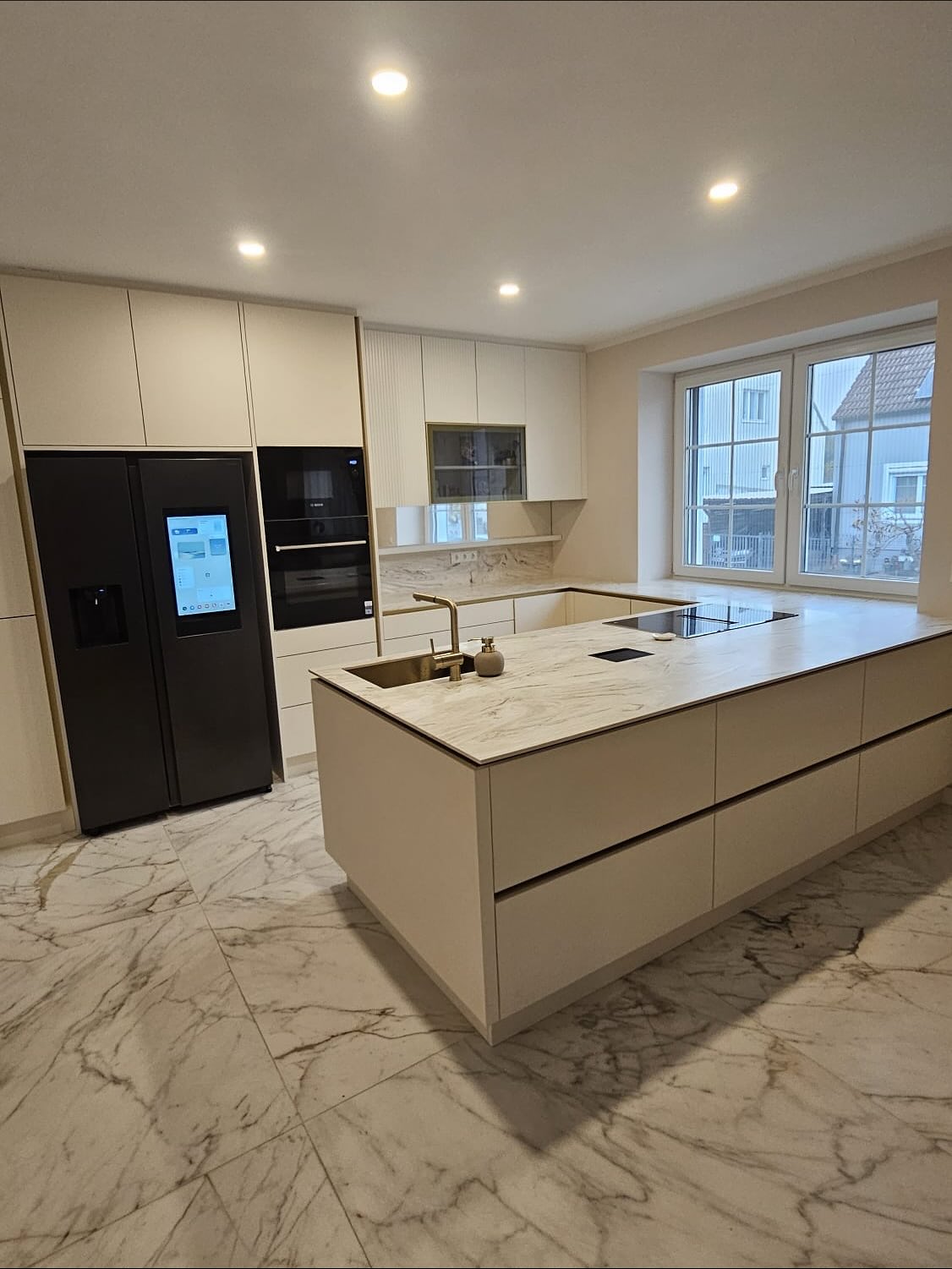 ✨ Modern. Elegant. Zeitlos. ✨ Diese großzügige Küche vereint warmes Beige mit edlen goldenen Akzenten – von den Griffleisten bis hin zum Alurahmen der Oberschränke. Die Corian-Arbeitsplatte fügt sich