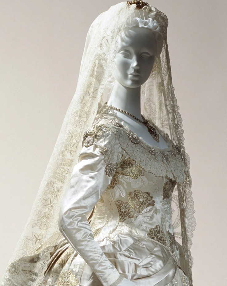 ivory brocade wedding dress A very regal gold and silk gown for an unnamed bride of 1882. It is lavishly trimmed with Brussels lace, silk tulle, faux pearls, and an entire skirt of returns-hidden