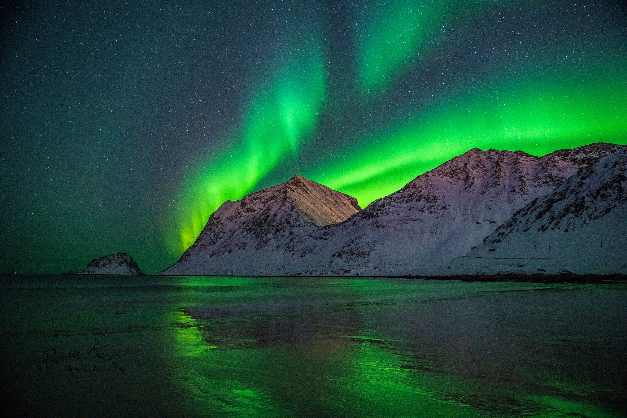 The Northern Lights shine over the rocks of Uttakleiv beach in