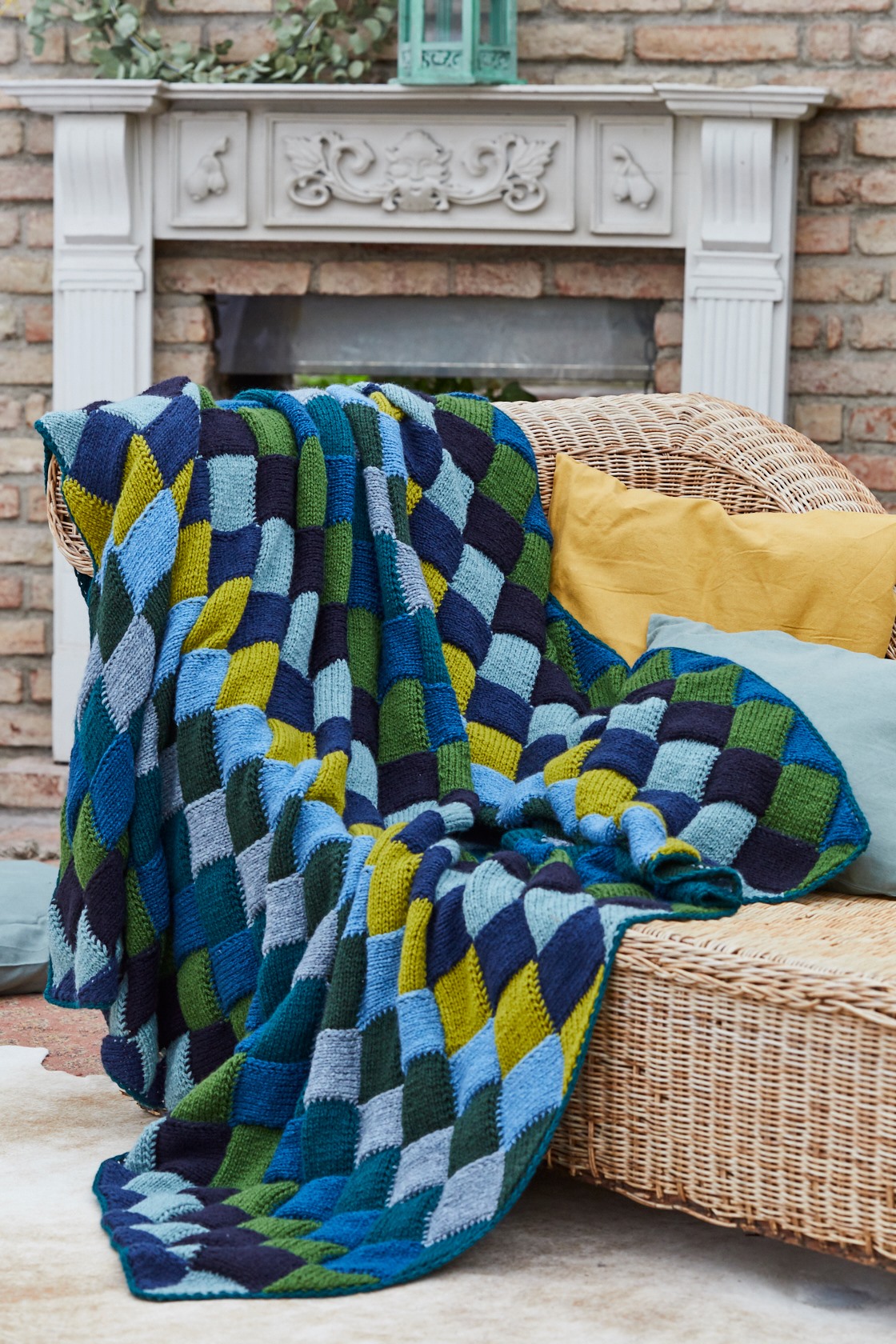 Diese Decke im Flechtmuster, dem sogenannten Entrelac, ist ein kleines Kunstwerk. Erst wird eine Reihe Dreiecke glatt rechts gestrickt. Daran werden Vierecke glatt rechts gearbeitet. Zehn Farben der L