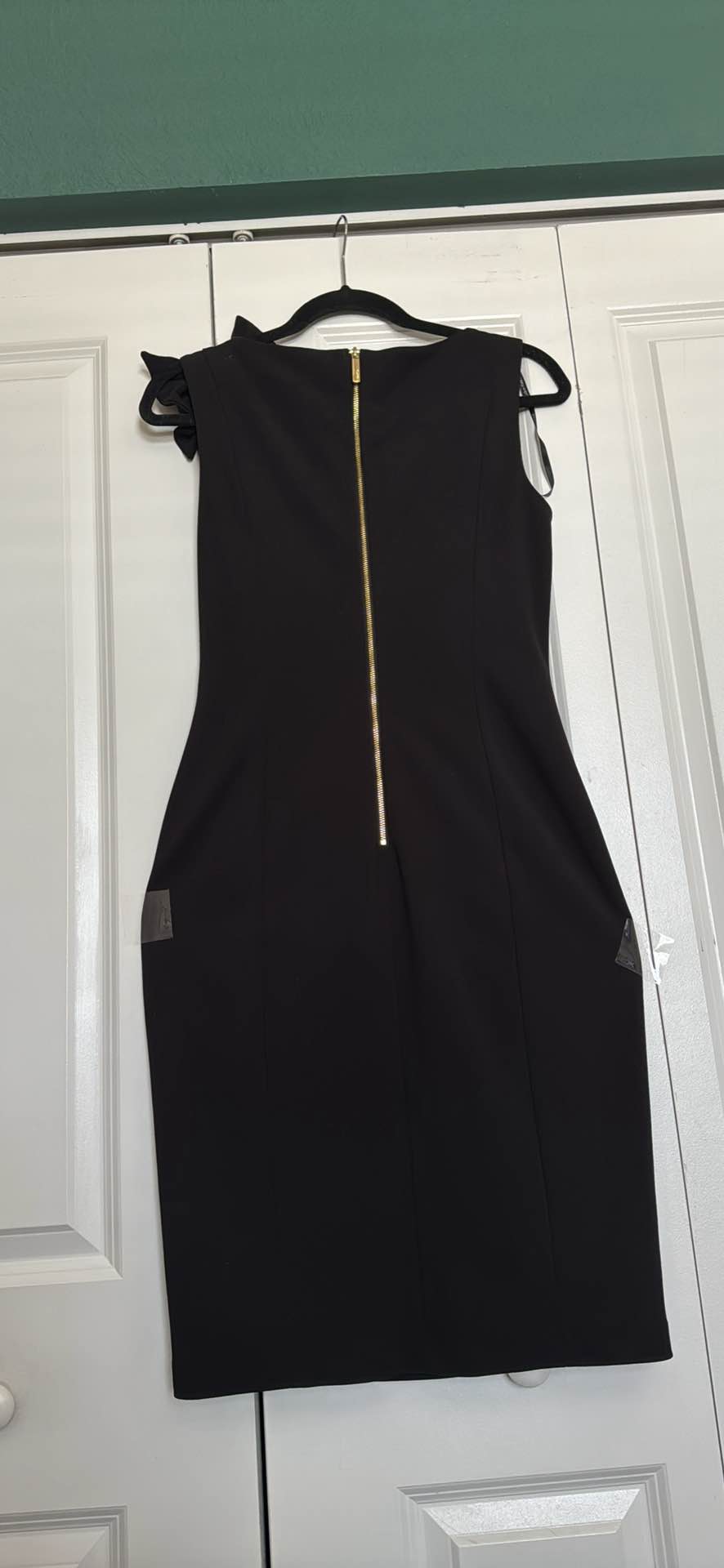 Elegant black Calvin Klein sleeveless sheath dress in size L. This garment has a ruffled detail on the left shoulder and a full-length gold-tone zipper closure at the back. The fabric is