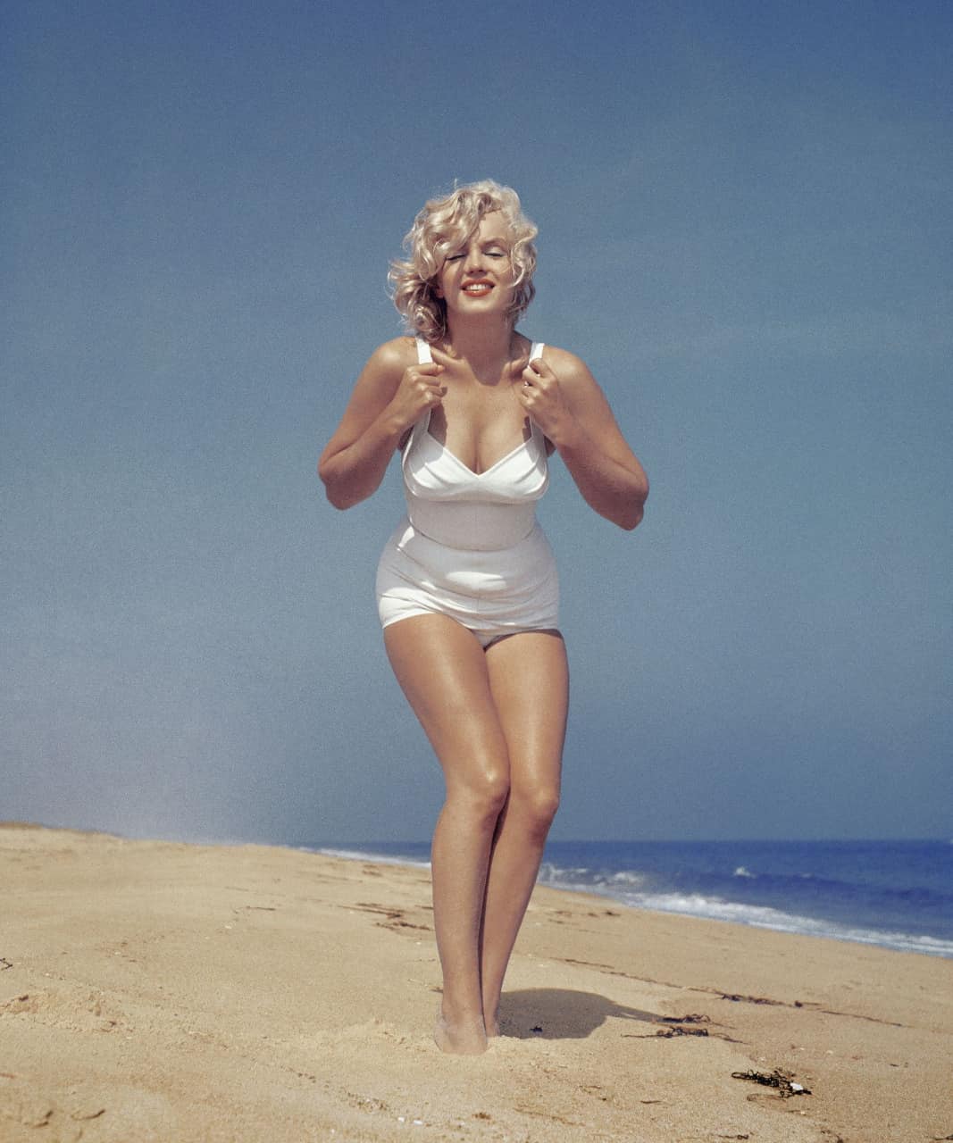 Marilyn Monroe lies on the beach at the edge of the water in 1957