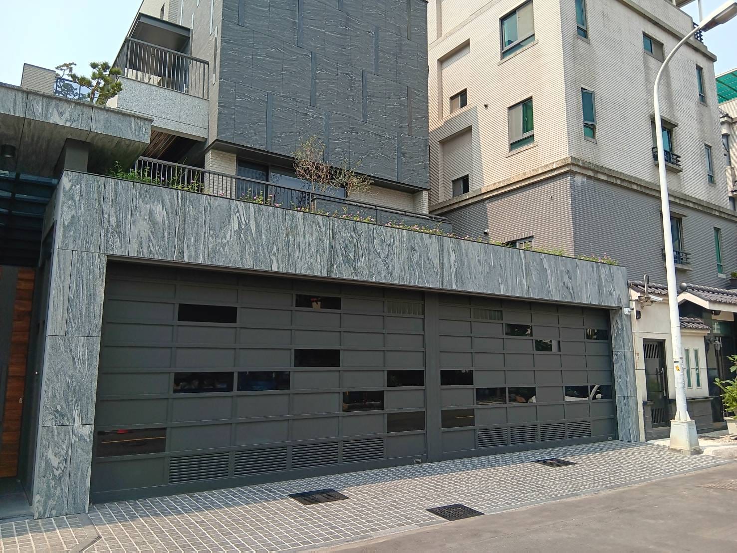 福麗門實業 - 位於台中市西屯區的案場 捲門選擇用鋁板及黑色噴砂玻璃以不規則幾何方式錯落設計 下方鑲嵌百葉增加通風性...