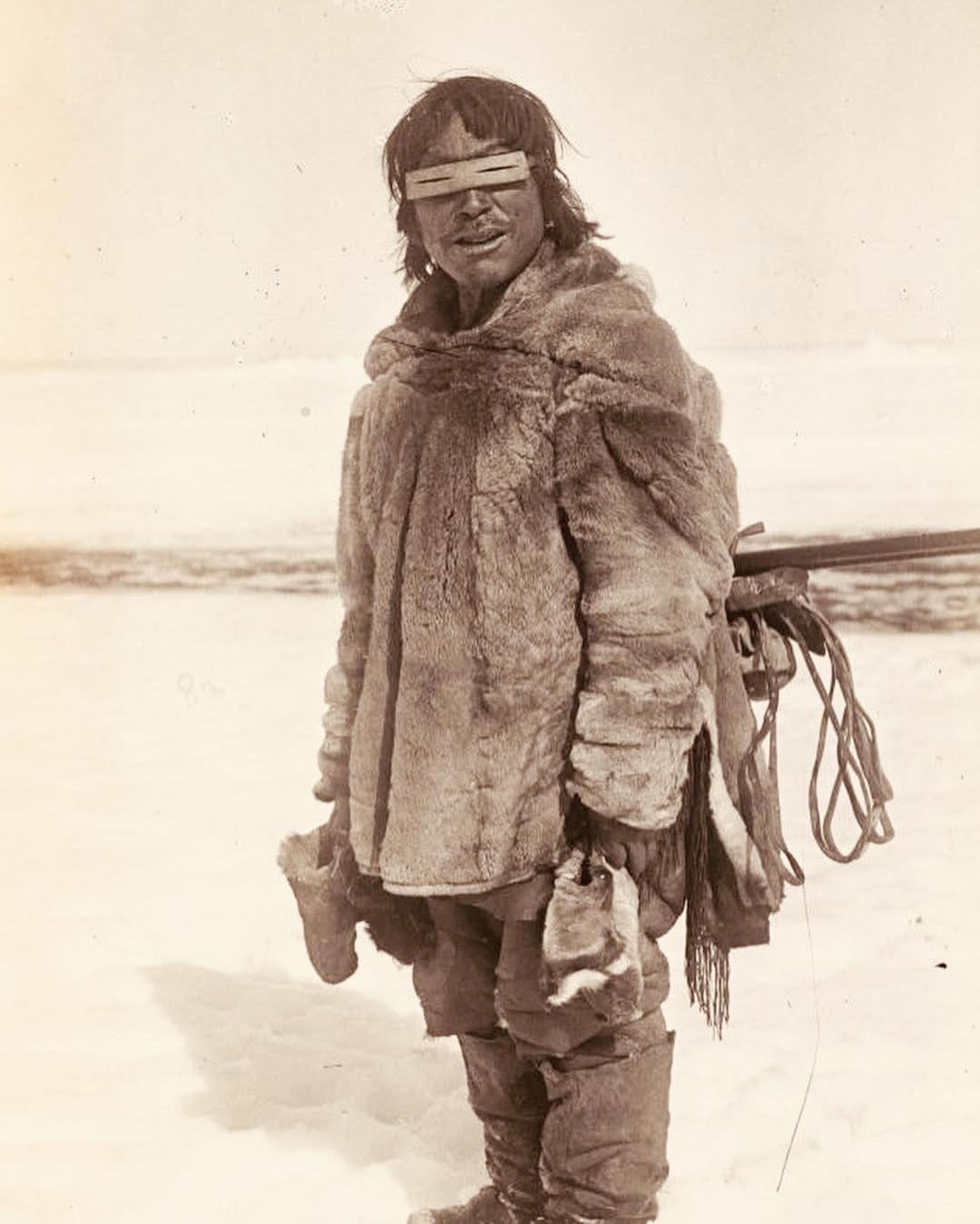An Inuk toddler in full furs holding onto a sled, taken likely in