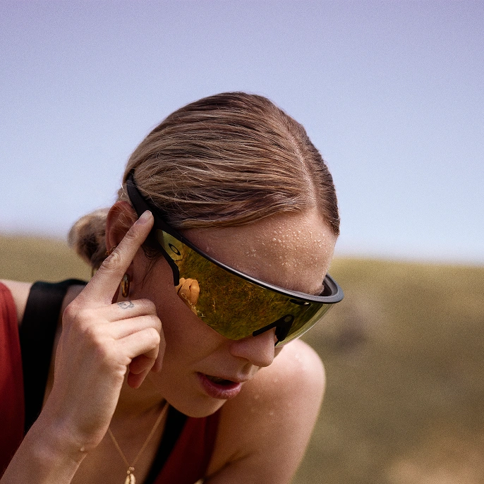 Woman wearing Oakley Meta glasses, pressing the right side of the glasses with her finger.