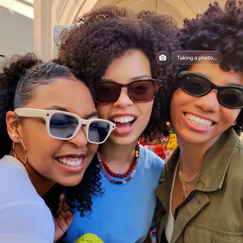Com o texto Tirando uma foto, três amigos tiram uma selfie juntos usando óculos inteligentes e sorrisos brilhantes.