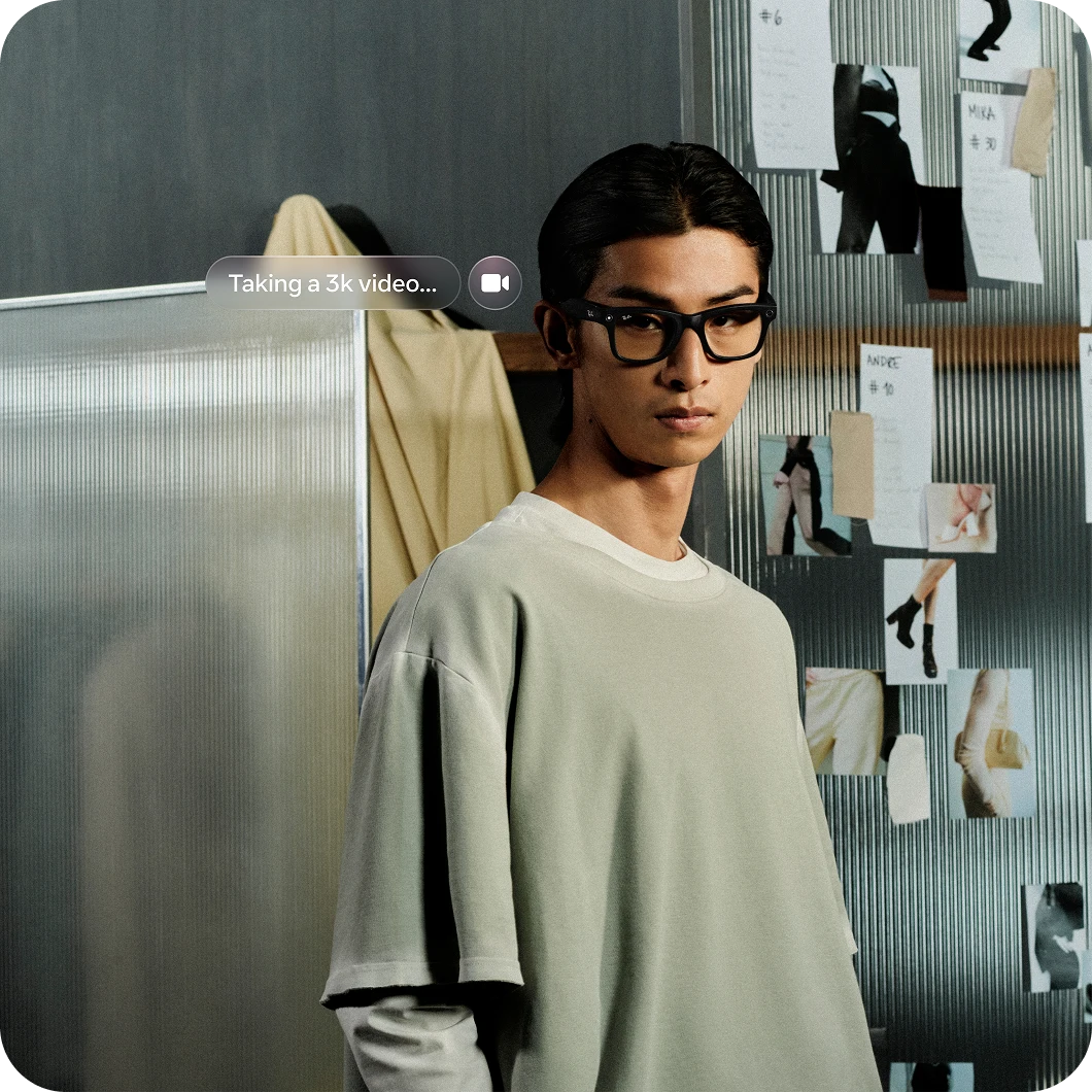 With text that reads "Taking a 3-second video". Person wears Ray-Ban Meta Wayfarer glasses by a studio bulletin board.