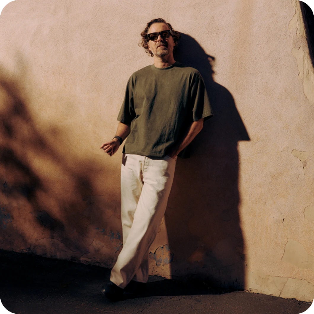 Person leaning against a sunlit wall outdoors wearing Ray-Ban Meta Wayfarer sunglasses with Shiny Black frame.